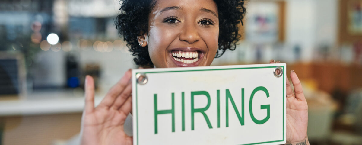 Woman hangs hiring sign and reflects on hiring trends as she thinks about attracting top candidates.